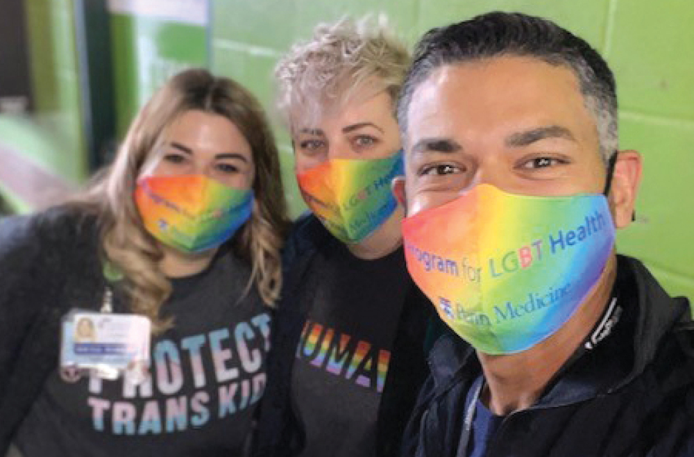 Three employees of Penn Medicine Lancaster General Health wear rainbow-colored facial masks at the event table for Lancaster Pride.